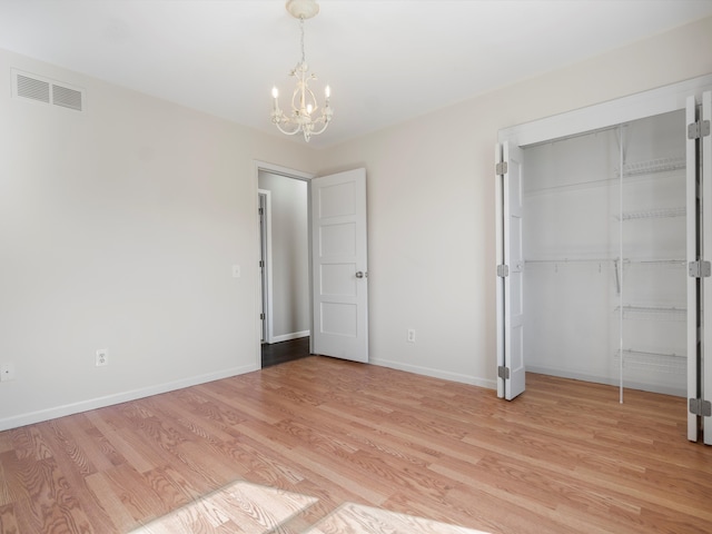 unfurnished bedroom featuring a notable chandelier, visible vents, light wood-style flooring, and baseboards