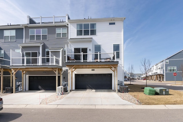 back of house featuring central air condition unit, a balcony, driveway, and a garage