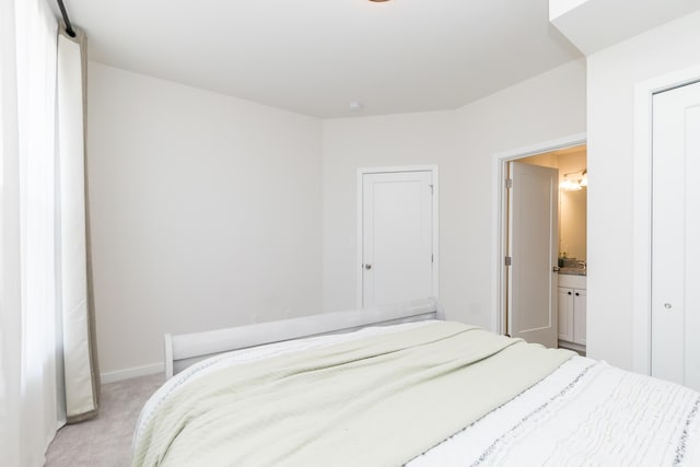 bedroom featuring baseboards, ensuite bathroom, and light carpet