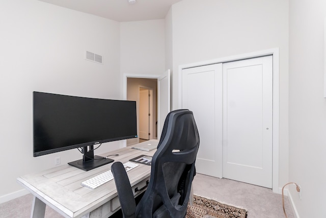 office space featuring visible vents, light carpet, baseboards, and a towering ceiling