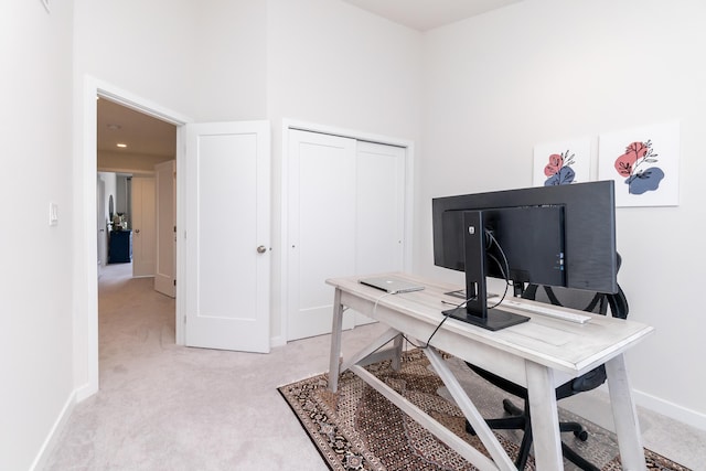 home office featuring light colored carpet, a high ceiling, and baseboards