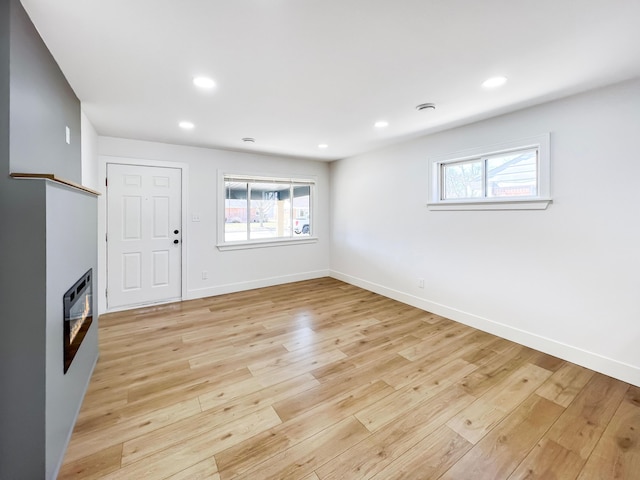 unfurnished living room with recessed lighting, light wood-type flooring, baseboards, and a glass covered fireplace