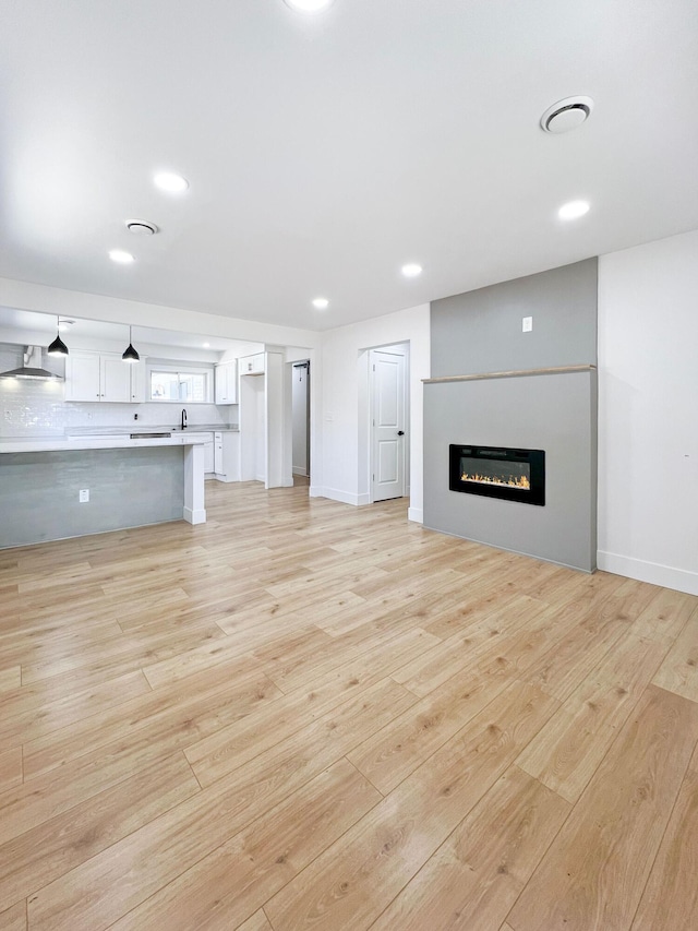 unfurnished living room featuring a glass covered fireplace, light wood-style flooring, recessed lighting, and baseboards