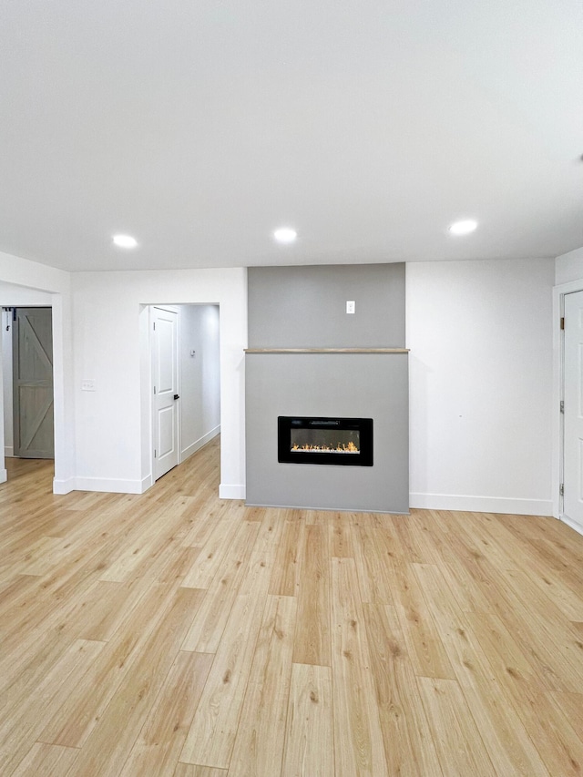 unfurnished living room with a glass covered fireplace, baseboards, and wood finished floors