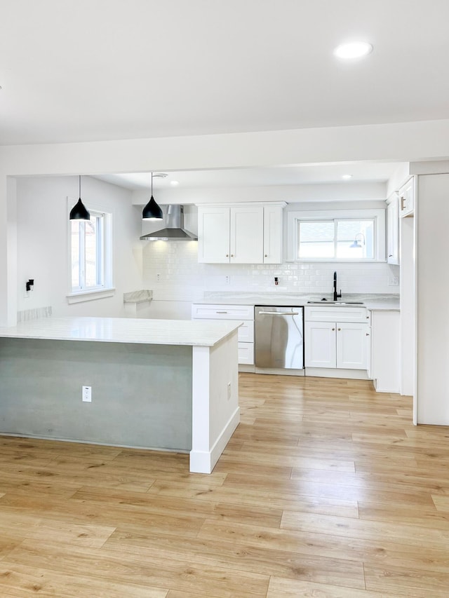 kitchen with a sink, white cabinets, light wood-style floors, dishwasher, and wall chimney range hood