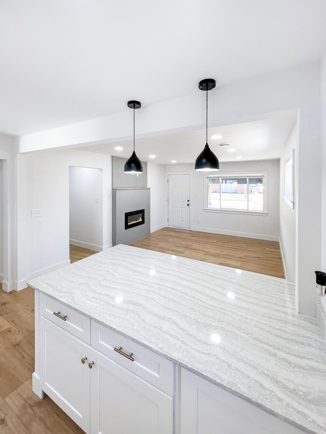 kitchen featuring light stone counters, light wood finished floors, hanging light fixtures, white cabinets, and open floor plan