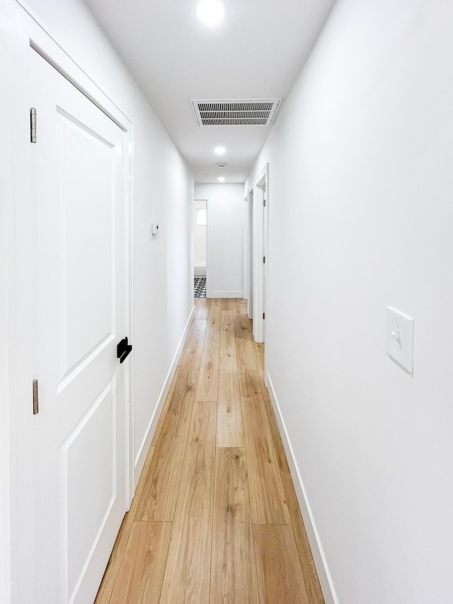 hallway with visible vents, light wood-style flooring, and baseboards