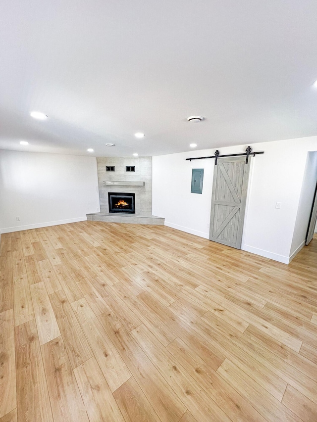 unfurnished living room featuring light wood-type flooring, recessed lighting, a barn door, a fireplace, and baseboards