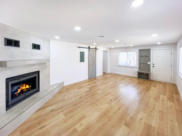 unfurnished living room featuring electric panel, a fireplace, recessed lighting, a barn door, and light wood-type flooring