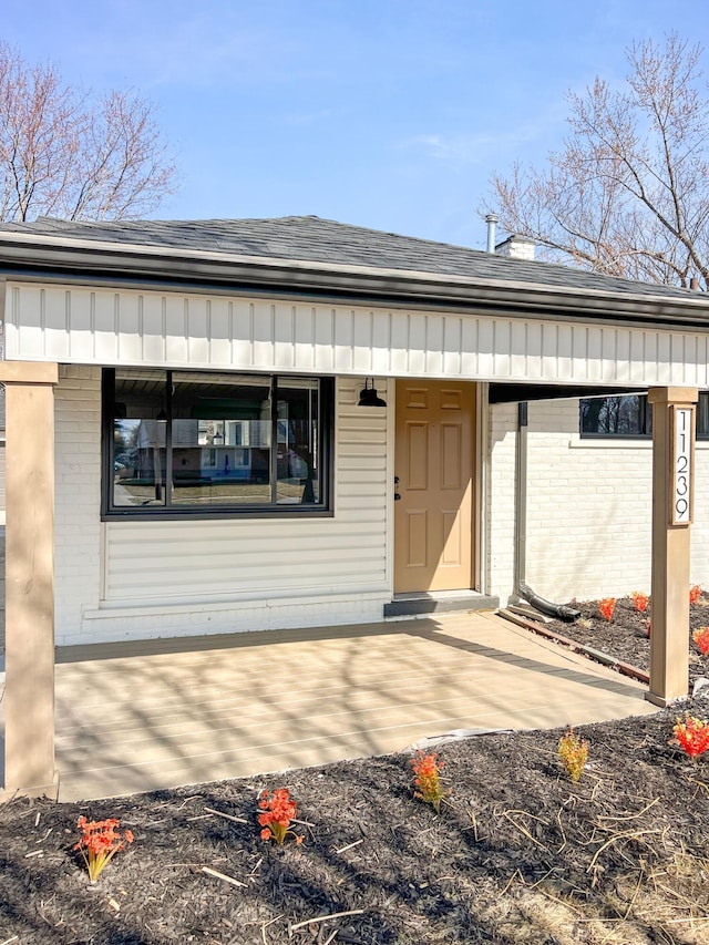 entrance to property with brick siding and a shingled roof