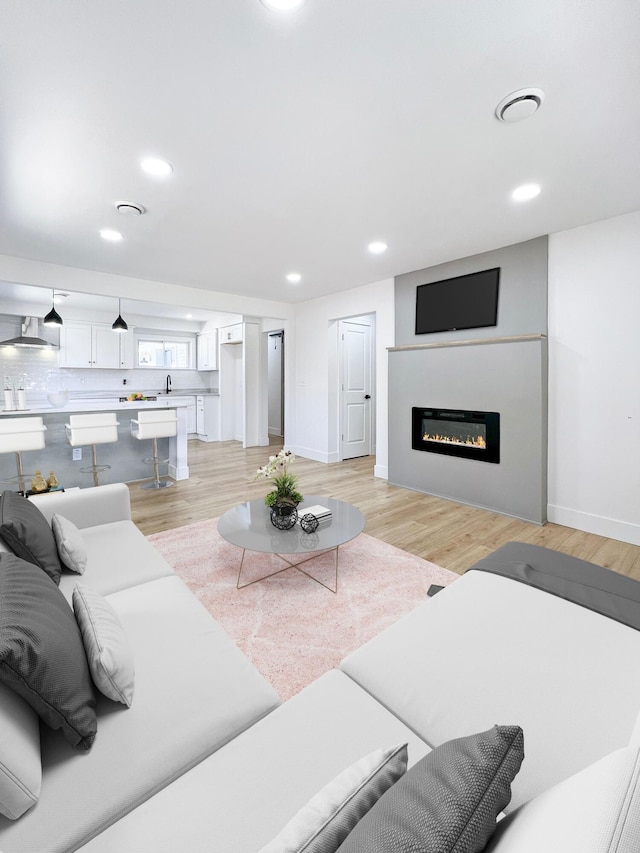 living room with a glass covered fireplace, recessed lighting, baseboards, and light wood finished floors