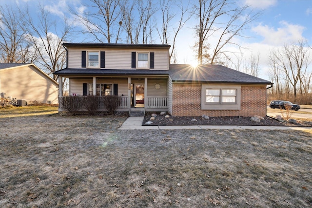 traditional-style house featuring a front yard, cooling unit, brick siding, and covered porch