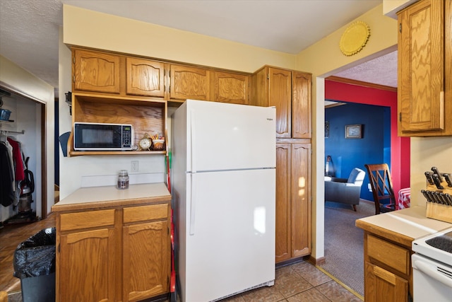 kitchen with white appliances, a textured ceiling, brown cabinetry, and light countertops