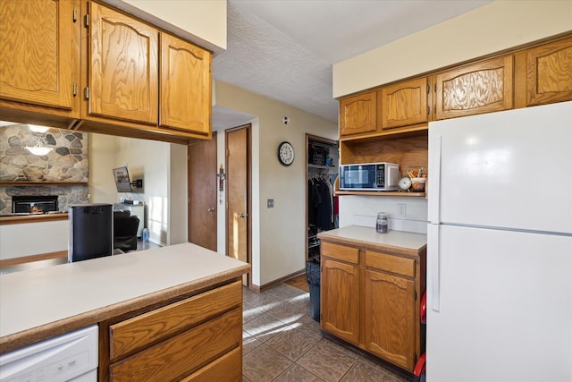 kitchen featuring white appliances, dark tile patterned flooring, a stone fireplace, light countertops, and a textured ceiling