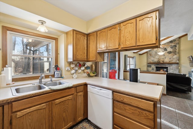 kitchen with a sink, a peninsula, a fireplace, light countertops, and dishwasher