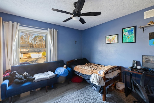 bedroom with a ceiling fan, wood finished floors, visible vents, and a textured ceiling