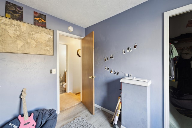 interior space featuring light wood-style flooring, a textured ceiling, and baseboards