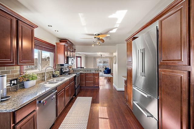 kitchen featuring tasteful backsplash, dark wood-type flooring, appliances with stainless steel finishes, a peninsula, and a sink