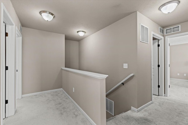 hall featuring an upstairs landing, visible vents, carpet flooring, and baseboards