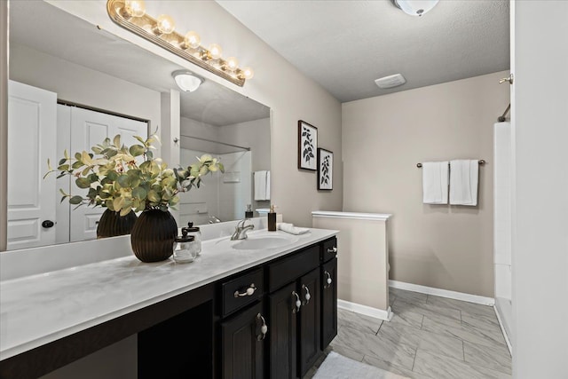 bathroom with marble finish floor, a textured ceiling, a shower, baseboards, and vanity