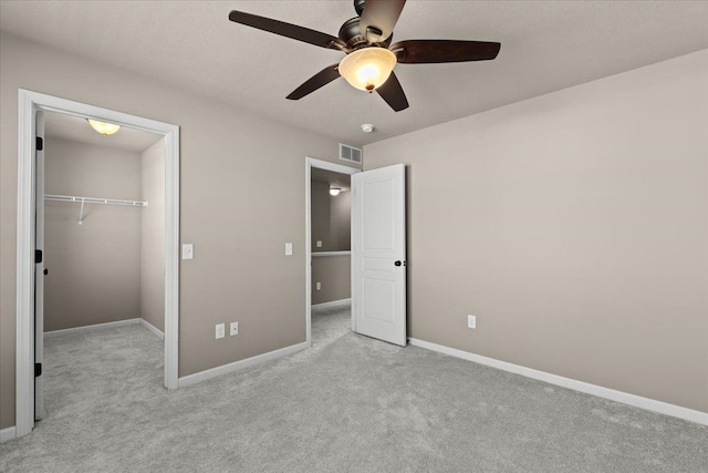 unfurnished bedroom featuring visible vents, a walk in closet, baseboards, light carpet, and a closet