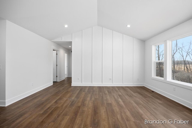 spare room featuring lofted ceiling, baseboards, and dark wood-style flooring