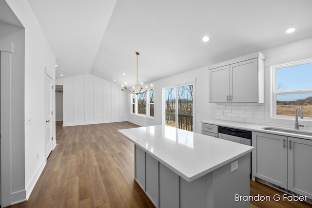 kitchen featuring a notable chandelier, gray cabinets, a sink, stainless steel dishwasher, and light countertops