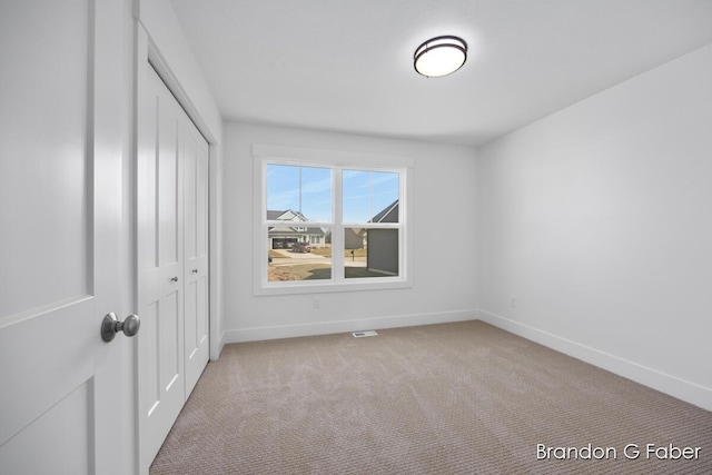 unfurnished bedroom featuring a closet, baseboards, light colored carpet, and visible vents