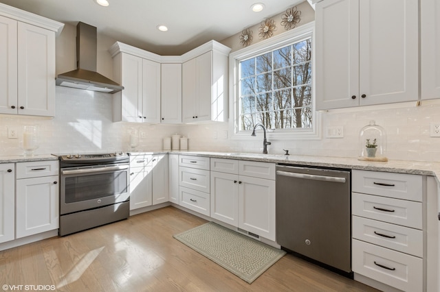 kitchen with light wood-style flooring, appliances with stainless steel finishes, wall chimney exhaust hood, and white cabinets