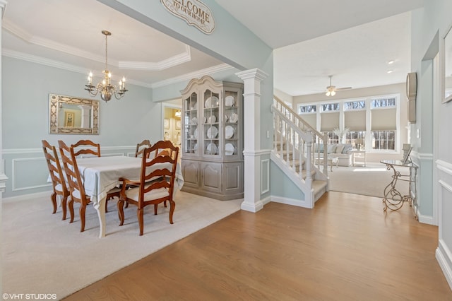 carpeted dining space featuring a raised ceiling, a decorative wall, ceiling fan with notable chandelier, and wainscoting