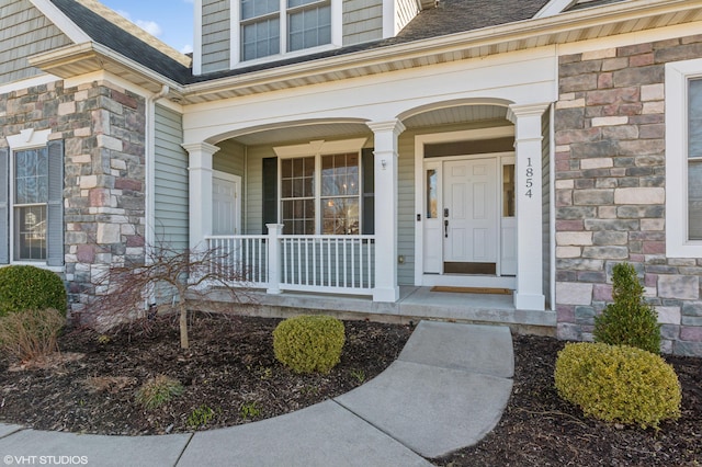 entrance to property featuring stone siding, covered porch, and a shingled roof