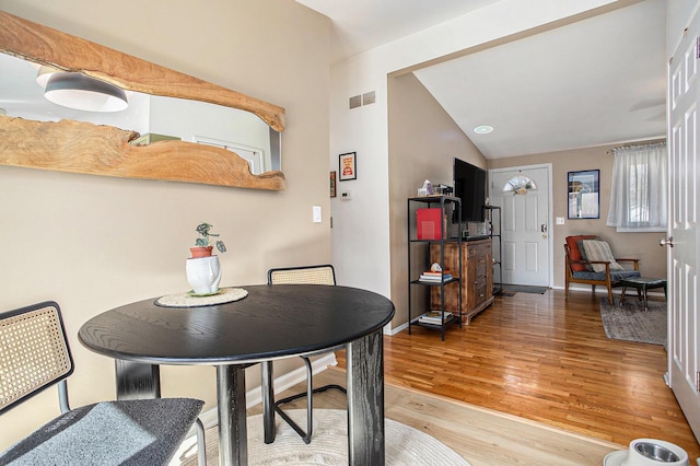 dining space featuring visible vents, baseboards, light wood-style floors, and vaulted ceiling