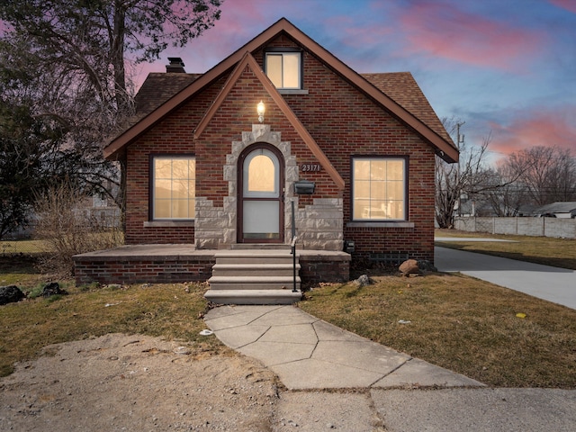 english style home with entry steps, brick siding, roof with shingles, and a chimney