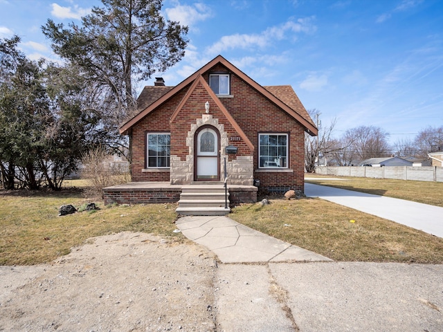 tudor home featuring a front lawn, concrete driveway, brick siding, and a chimney