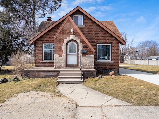 tudor home featuring a shingled roof, entry steps, a front lawn, a chimney, and brick siding