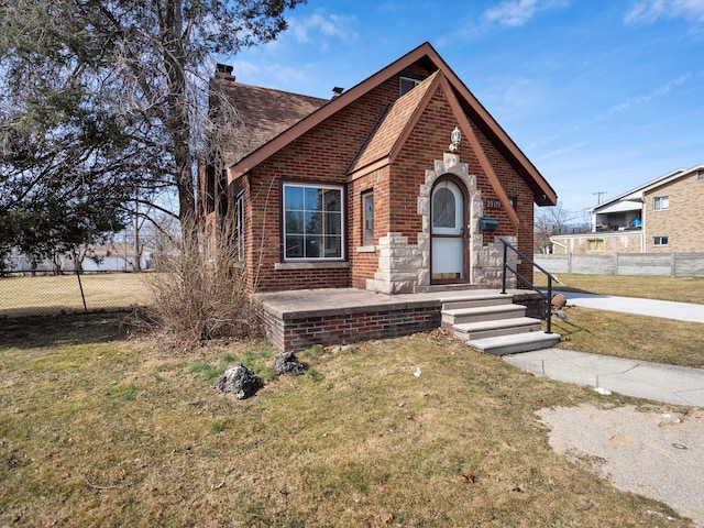 view of front of property with brick siding, a front lawn, fence, roof with shingles, and a chimney