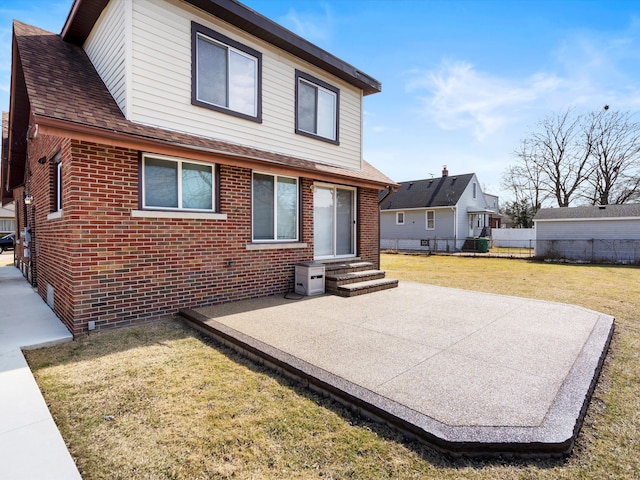 rear view of house featuring fence, roof with shingles, a yard, entry steps, and brick siding