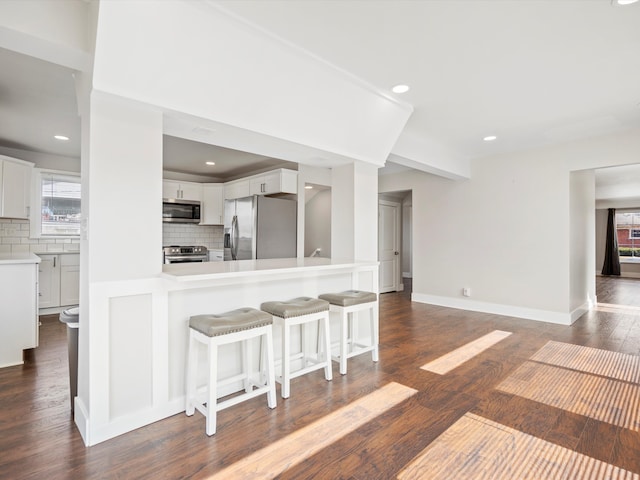 kitchen featuring white cabinetry, dark wood-style flooring, appliances with stainless steel finishes, a kitchen bar, and tasteful backsplash