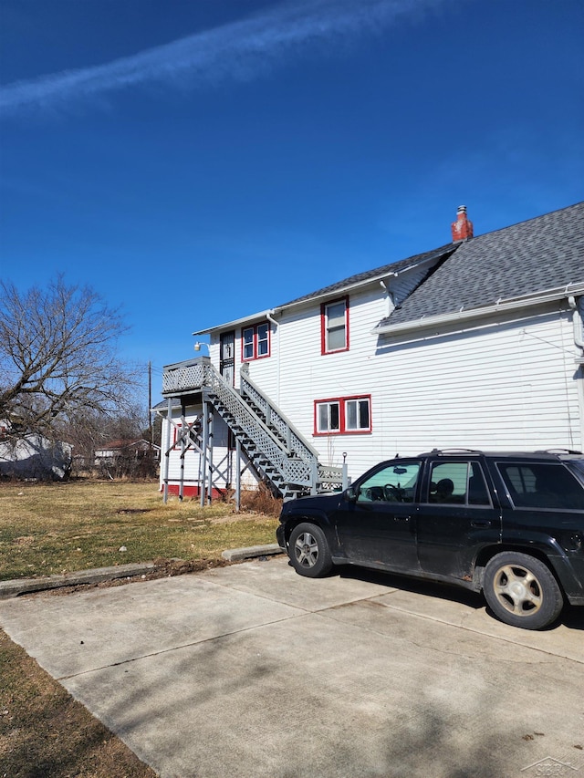 exterior space featuring stairway, a chimney, roof with shingles, and a front lawn