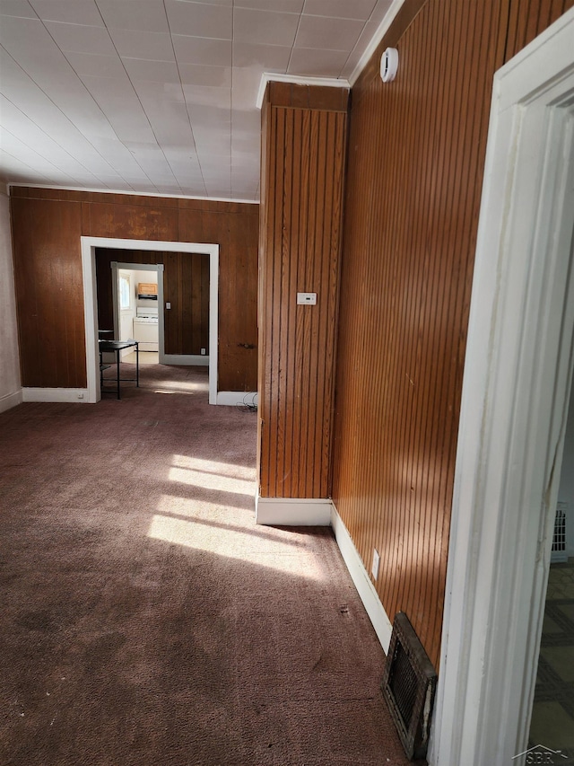 hallway with wooden walls, carpet flooring, baseboards, and visible vents