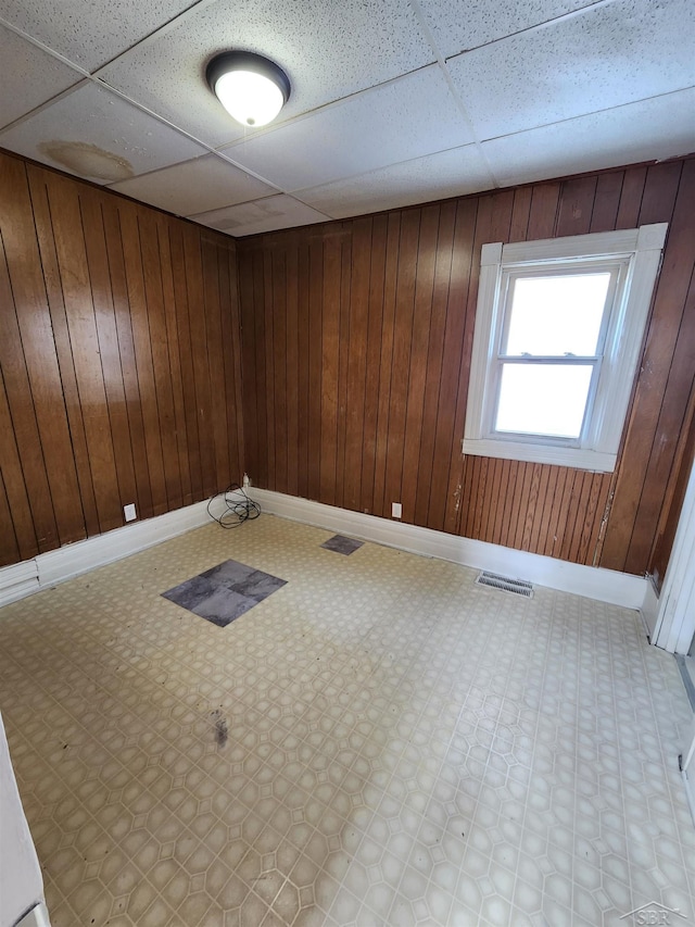 empty room featuring a drop ceiling, baseboards, visible vents, and wood walls