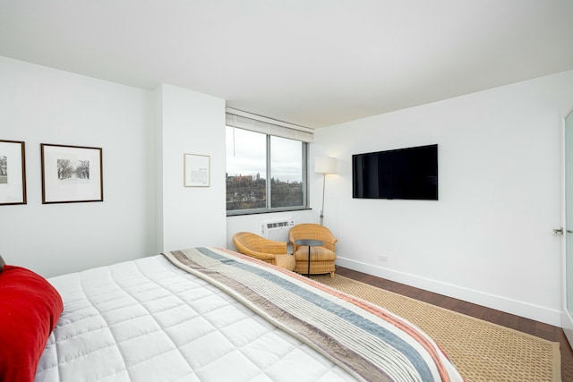 bedroom featuring baseboards, wood finished floors, and a wall mounted AC