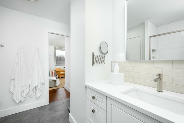 bathroom featuring vanity, wood finished floors, baseboards, ensuite bathroom, and tasteful backsplash