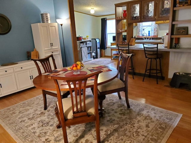 dining space featuring a textured ceiling, light wood-type flooring, and ornamental molding