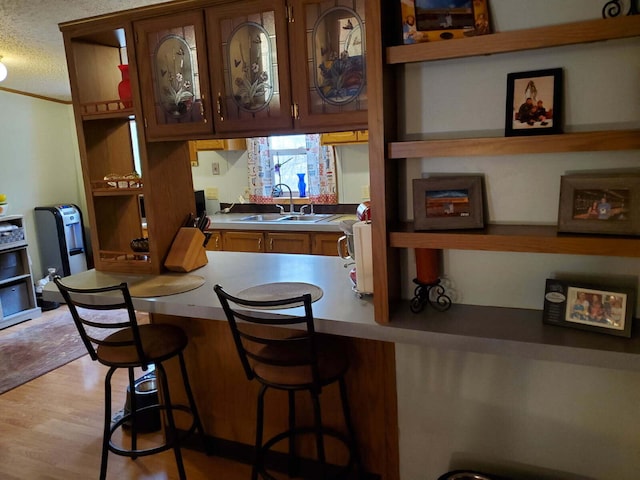 kitchen with a sink, light wood-type flooring, a textured ceiling, and a breakfast bar area