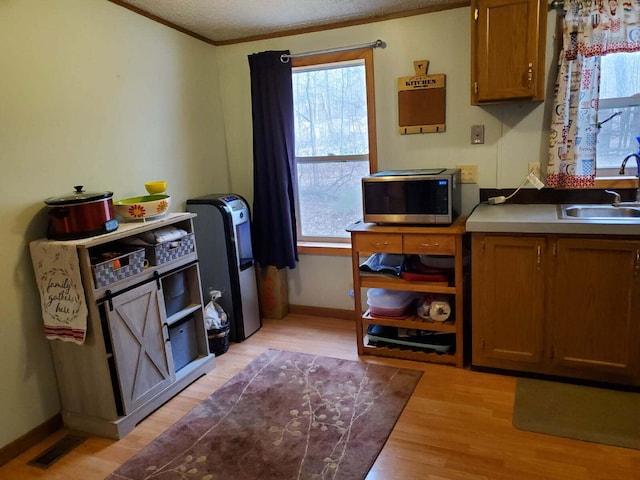 kitchen featuring visible vents, a sink, crown molding, stainless steel microwave, and light wood-type flooring