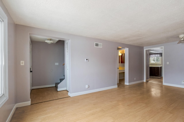 unfurnished living room with visible vents, baseboards, stairs, light wood-style flooring, and a textured ceiling