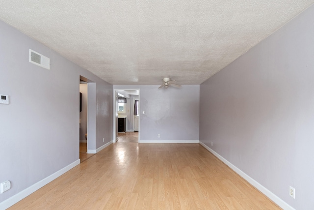 empty room with light wood-type flooring, visible vents, a ceiling fan, a textured ceiling, and baseboards