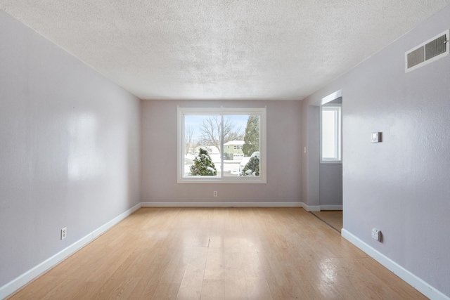 spare room featuring light wood-style flooring, baseboards, visible vents, and a textured ceiling