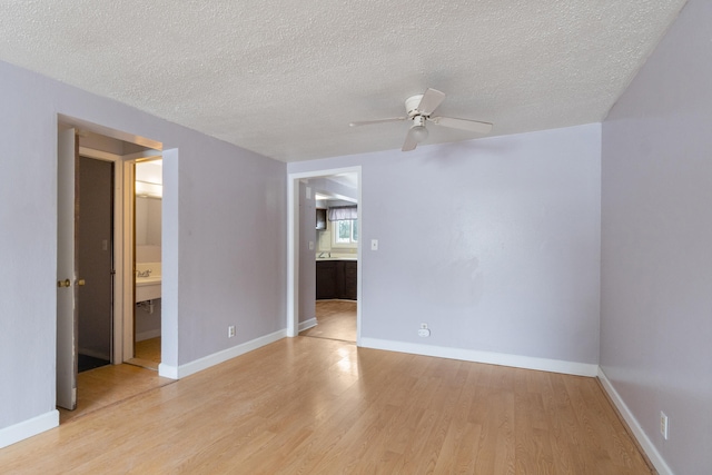 spare room with a textured ceiling, baseboards, light wood-type flooring, and ceiling fan